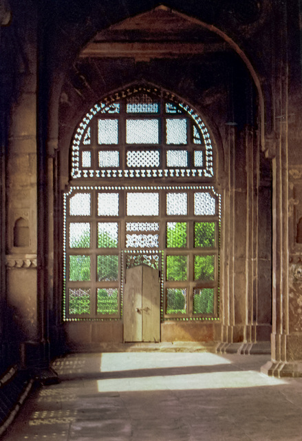Photograph of lofty building hallway with high arched windows made from marble lattice carved with intricate geometric designs; garden beyond.